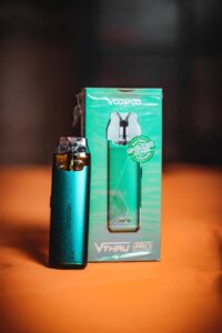 Voopoo Vthru Pro pod vape kit in teal beside its matching green product box on an orange surface.